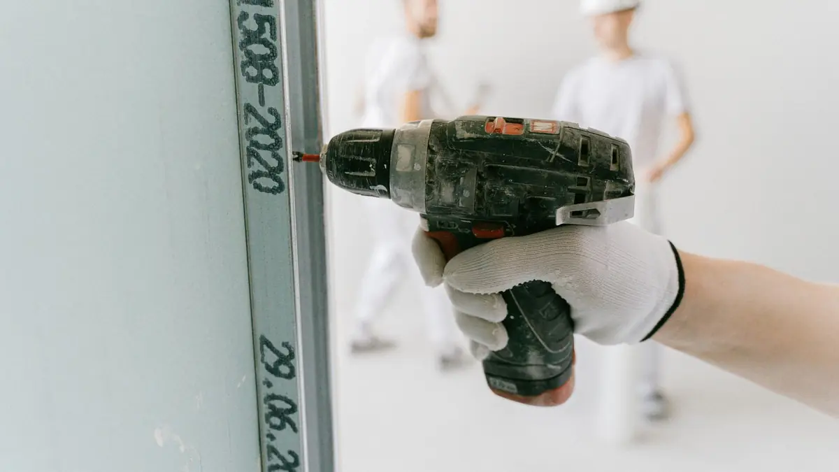 A drywall installer fastening a sheet to the wall framing