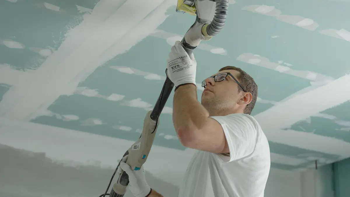 A worker sanding a smooth ceiling with a pole sander